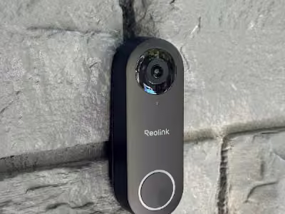 Black Reolink video doorbell on a painted brick wall.