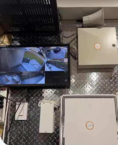 Security monitor, alarm enclosures and network equipment on a metal-panelled wall.