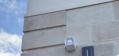 White outdoor security camera on a grey brick wall.