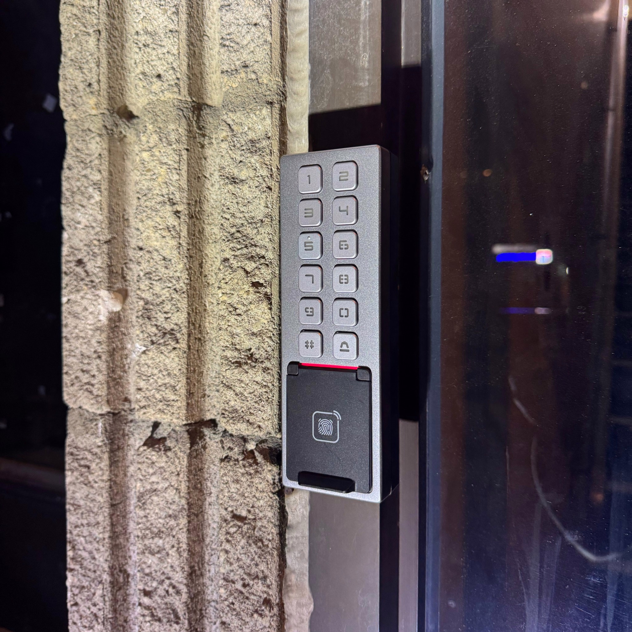 Access control keypad and fingerprint reader installed beside a glass door