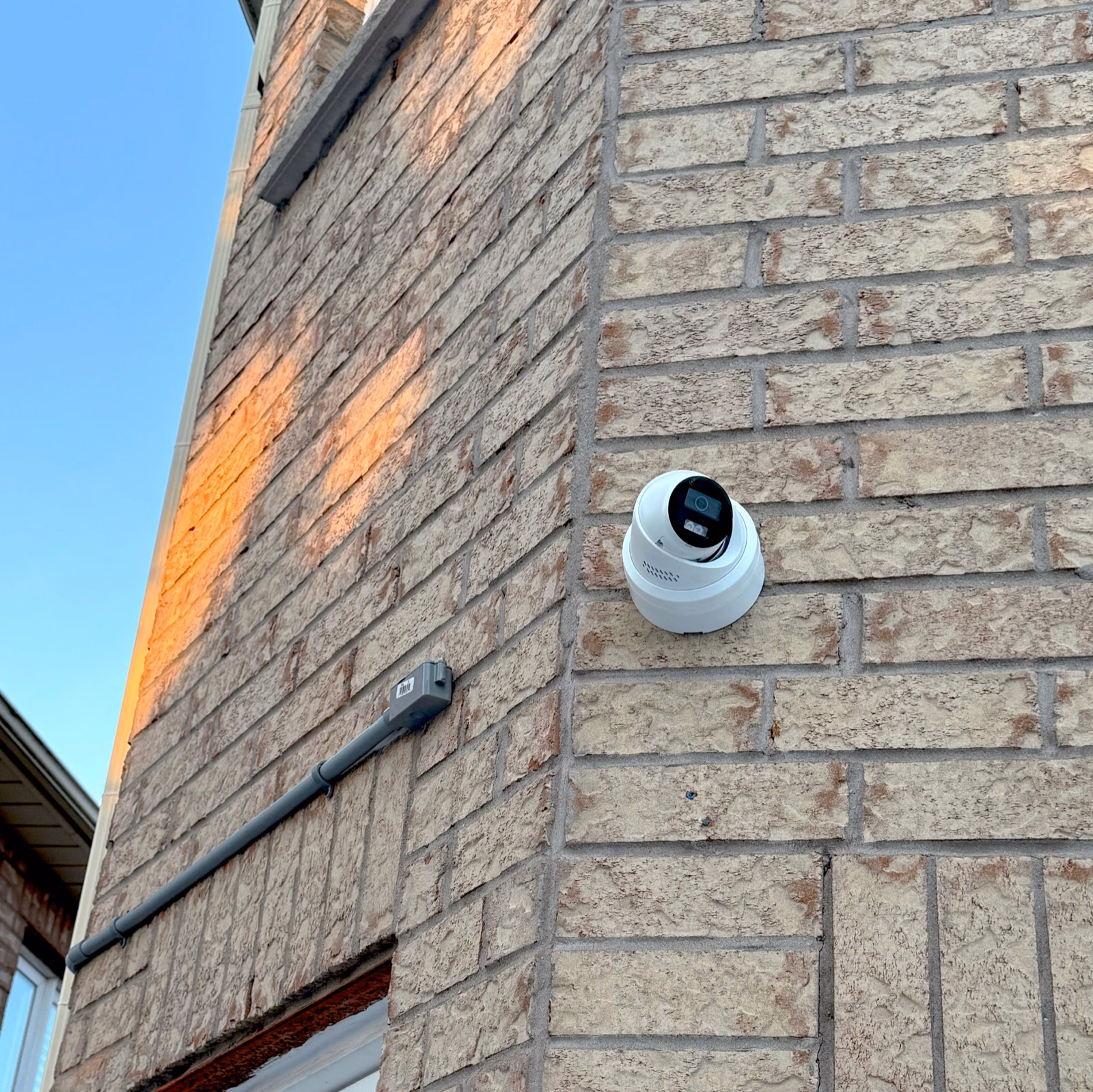 Security camera mounted on a brick wall beside conduit