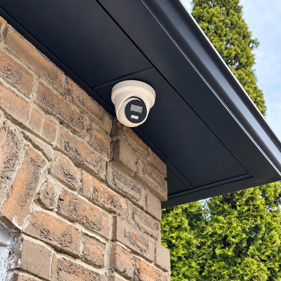 Wired security camera mounted beneath a dark soffit on a stone wall