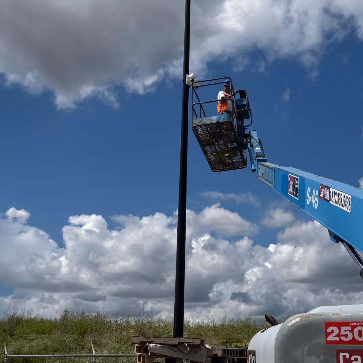 Boom lift raised beside a security camera pole