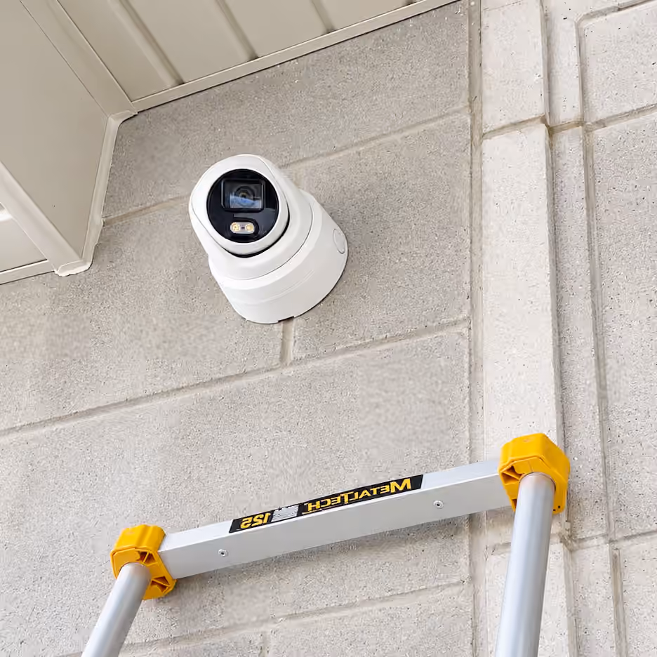 Security camera mounted on an exterior wall above an installation ladder