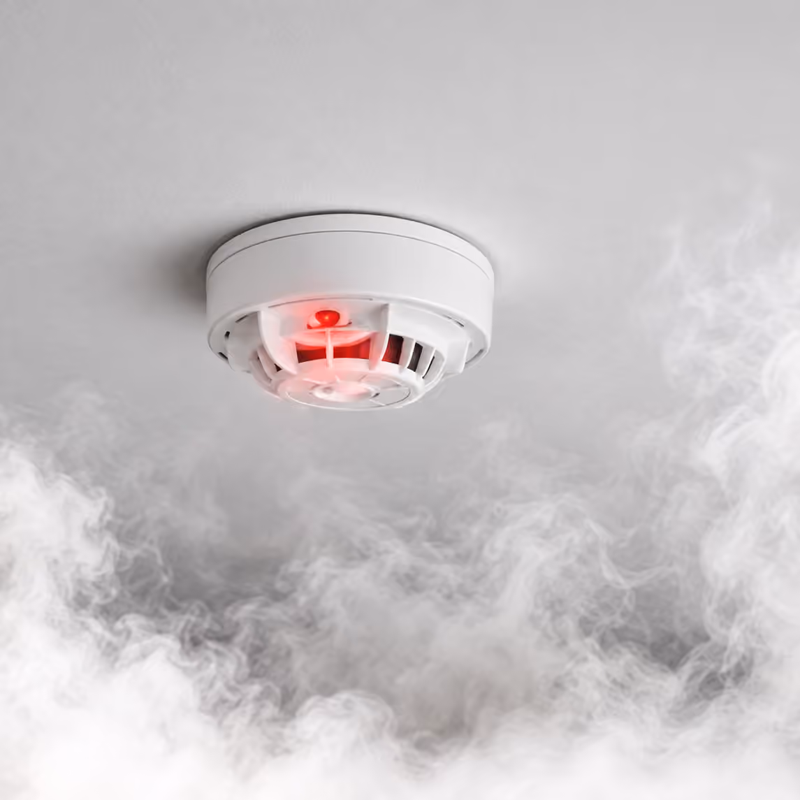 Ceiling smoke detector with a red indicator surrounded by drifting smoke